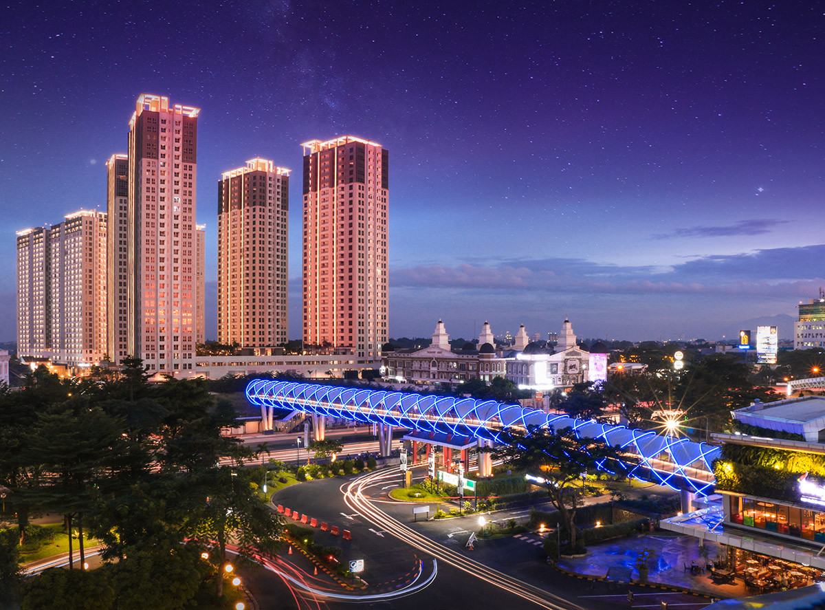 M-Town Residence towers lit at dusk with an illuminated footbridge in the foreground