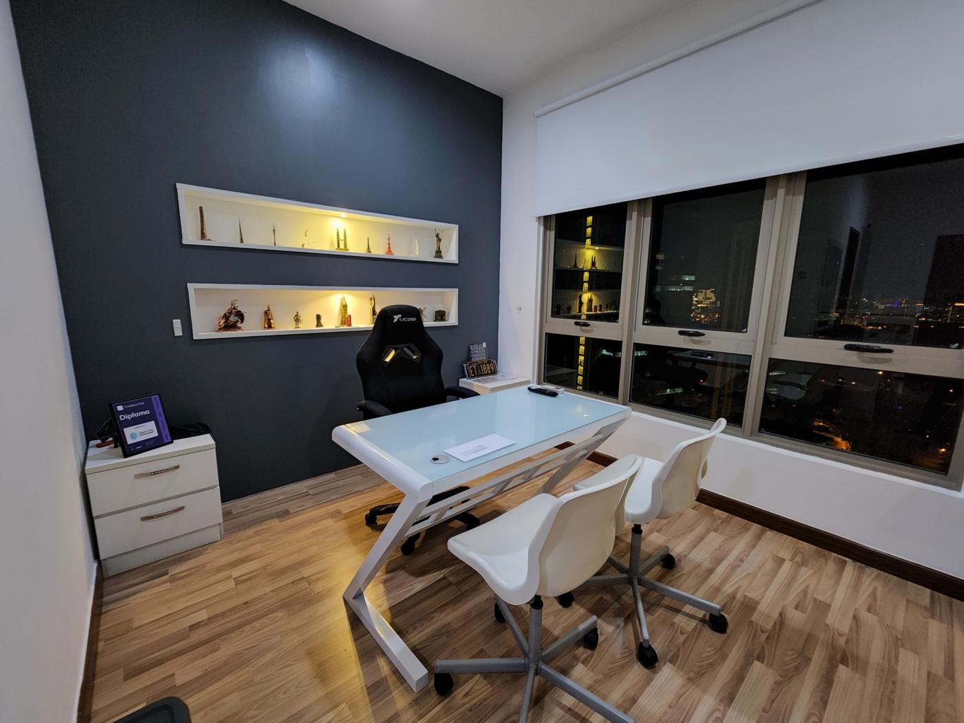 Work room with a glass-top desk, illuminated display shelves and a city view at night