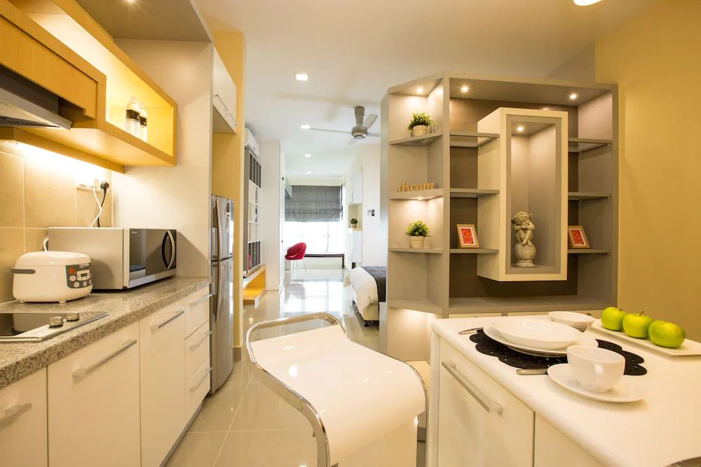 Furnished studio in Cyberjaya with a fitted kitchen, shelving and a bed beyond